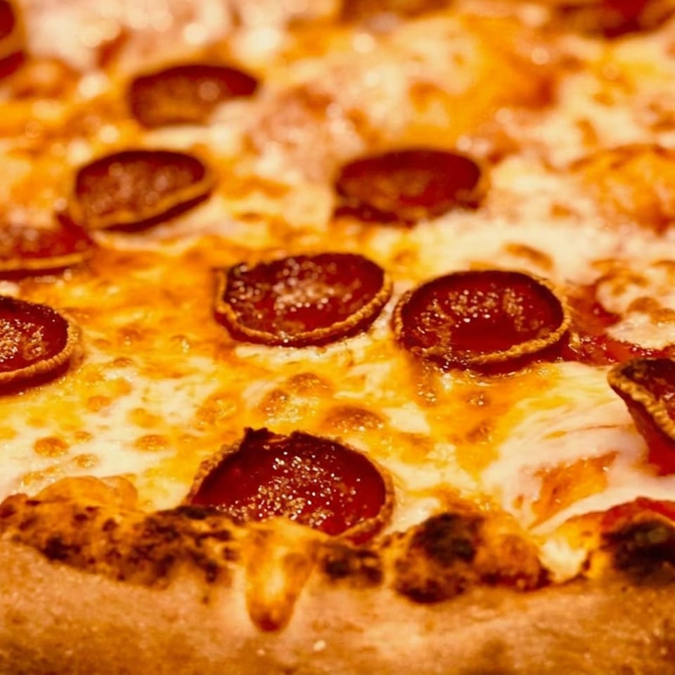 Close-up of a pepperoni pizza with melted cheese and a charred, golden-brown crust.