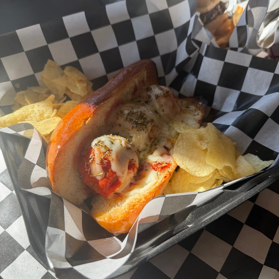 Cheesy toasted sandwich with tomato and herbs served alongside potato chips in a black-and-white checkered basket.