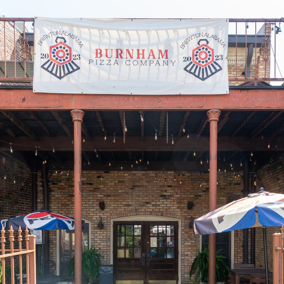 Brick patio entrance to Burnham Pizza Company in Birmingham, Alabama, with a large restaurant banner, umbrellas, and string lights.